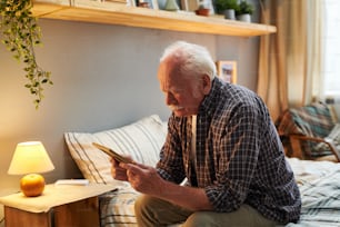 Uomo anziano seduto sul letto in camera da letto e guardando la foto nella cornice, gli manca la sua famiglia