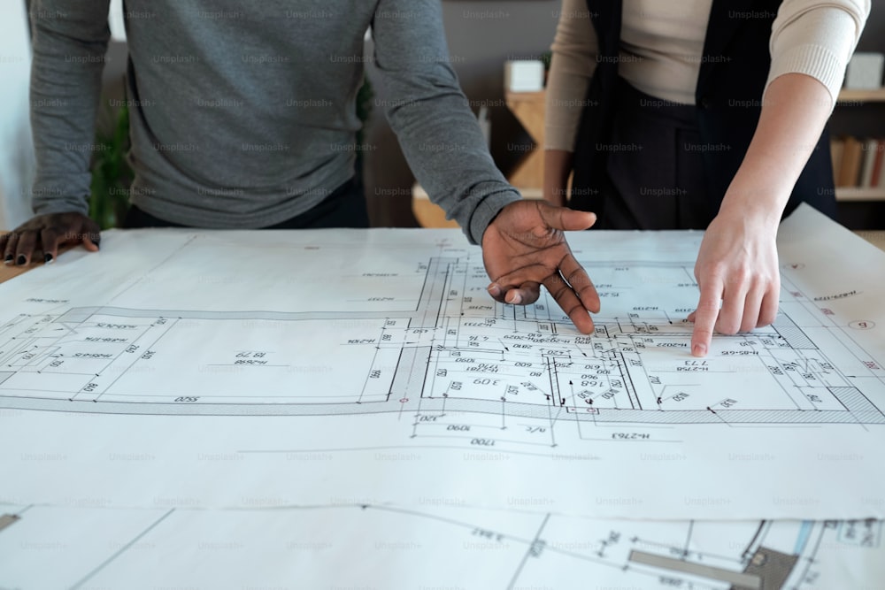 Hände zweier interkultureller Architekten, die auf eine Skizze zeigen, die ein neues Bauprojekt oder einen Stadtteil darstellt
