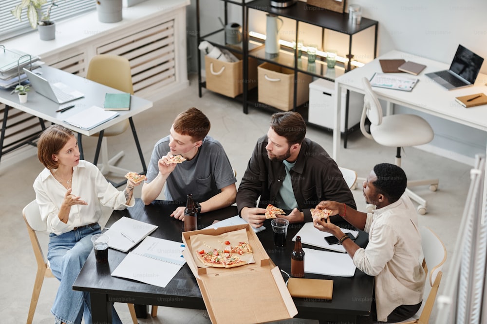 High angle view of business colleagues eating pizza and drinking beer at the table during corporate at office