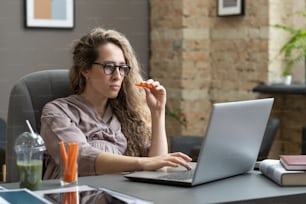 Elegant pregnant businesswoman with carrot looking at laptop screen while looking through online information in office