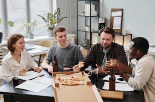 Group of business people eating pizza drinking beer and talking together at the table during party at office after work