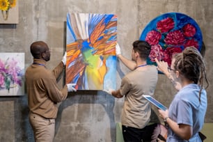 Dos jóvenes cuelgan pintura abstracta en la pared mientras se preparan para la presentación de una nueva colección de obras de arte