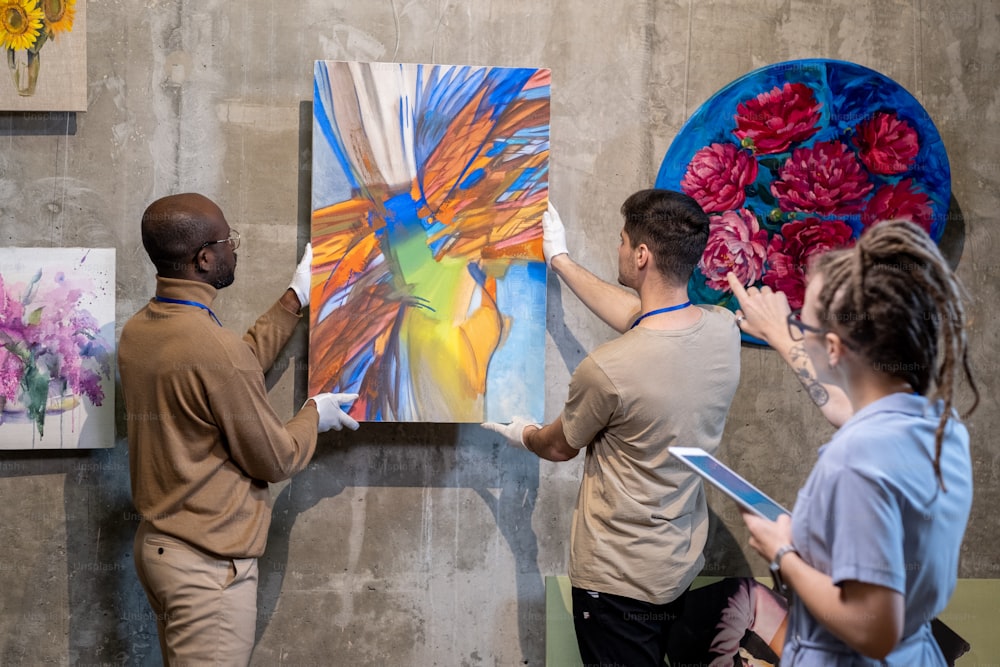 Due giovani che appendono il dipinto astratto al muro mentre si preparano per la presentazione della nuova collezione di opere d'arte