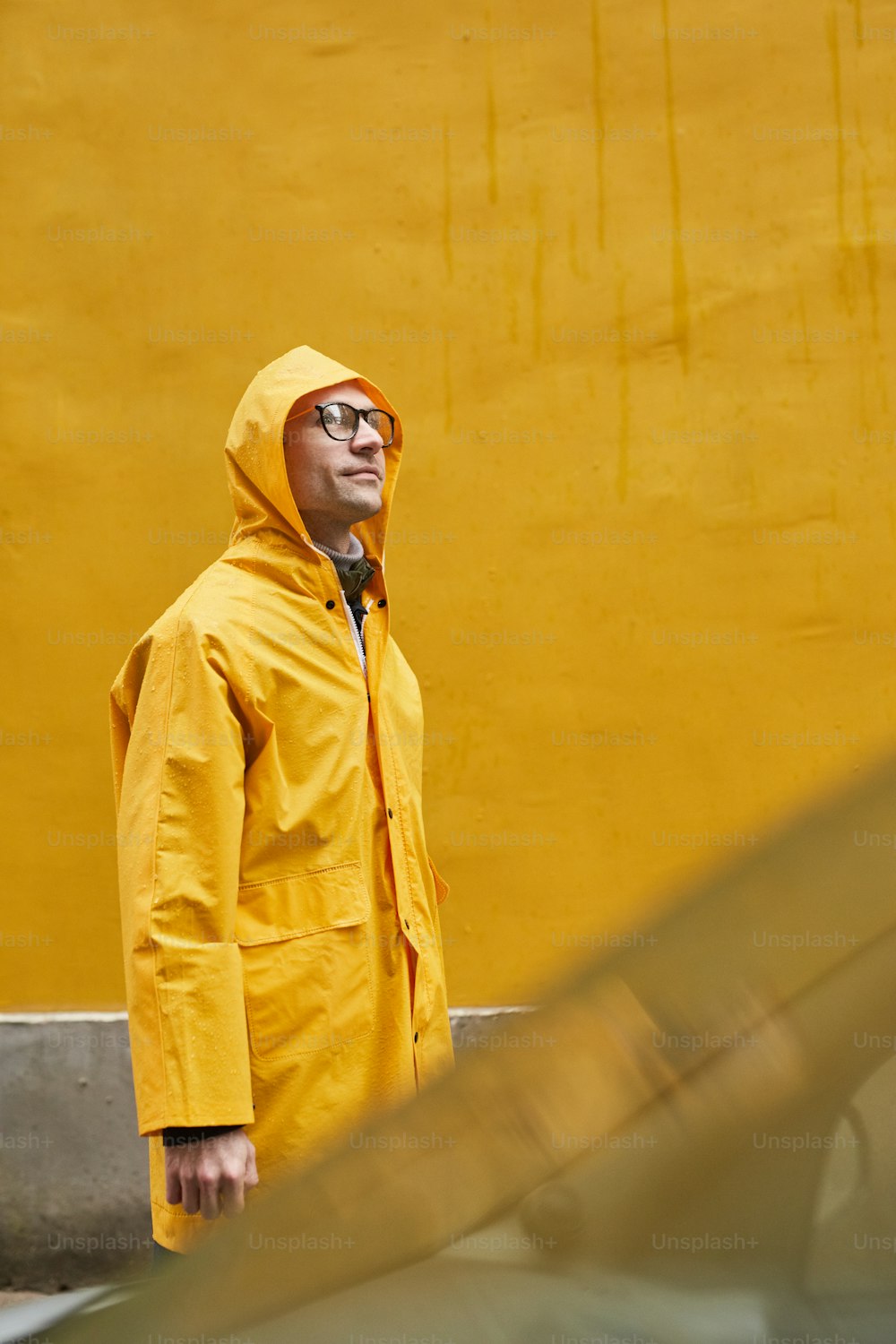 黄色いレインコートを着た成熟した白人男性が雨の中を歩いている縦方向のミディアムロングショット