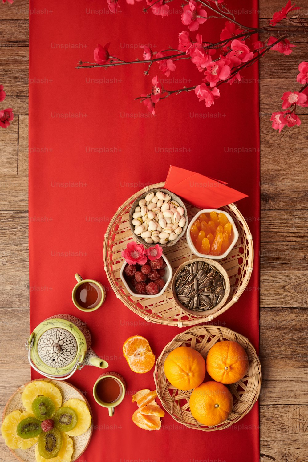 Kandierte Früchte, Nüsse, Mandarinen und Tee auf roter Tischdecke, serviert für die Tet-Feier, Blick von oben