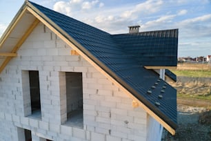 Aerial view of unfinished house with aerated lightweight concrete walls and wooden roof frame covered with metallic tiles under construction.