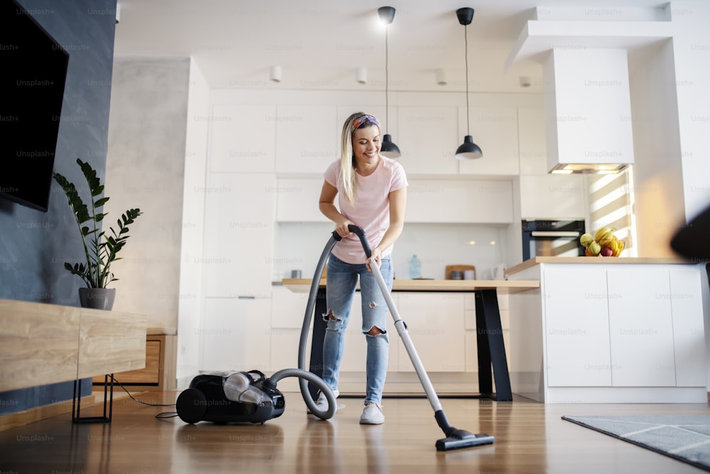 웃고 있는 여자가 집 거실 바닥을 진공 청소기로 청소하고 있다.