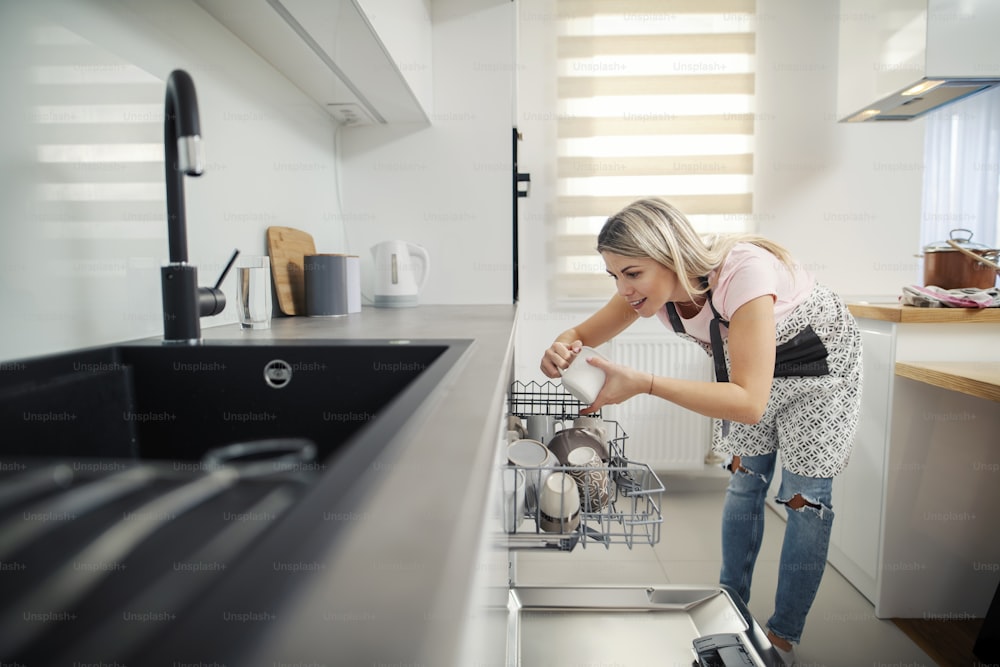 Una mujer ordenada poniendo platos en un lavavajillas en su cocina.