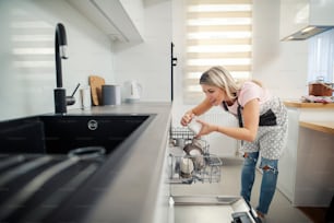 Uma mulher arrumada colocando pratos em uma máquina de lavar louça em sua cozinha.
