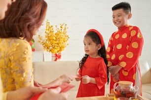 Hermano y hermana pequeños recibiendo sobres rojos que simbolizan la buena suerte para el Año Nuevo Lunar
