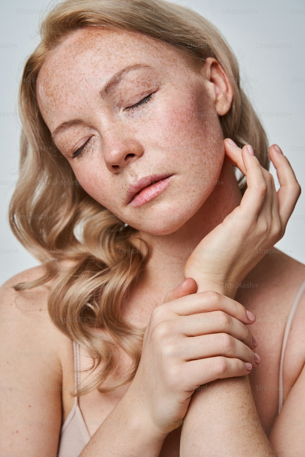 Vertical portrait of young pretty caucasian lady with freckled skin standing opposite camera and closed her eyes in studio. Beauty, facial treatment and spa concept