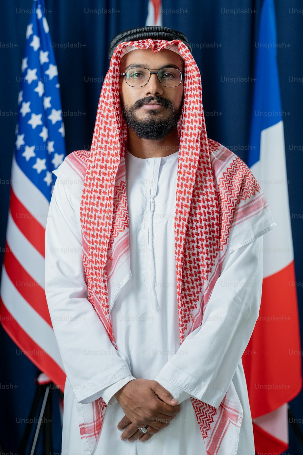 Young Arabian man in turban and national clothes keeping hands put together while standing in front of camera