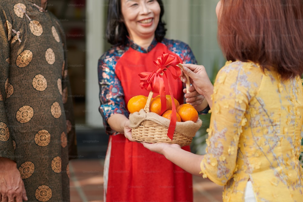 Frau schenkt ihren älteren Eltern einen dekorierten Korb mit Mandarinen zur Tet-Feier