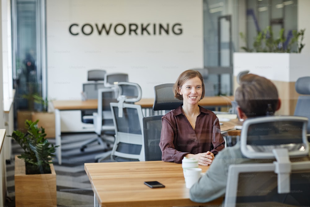 Portrait of smiling young woman in job interview at office behind glass wall, copy space