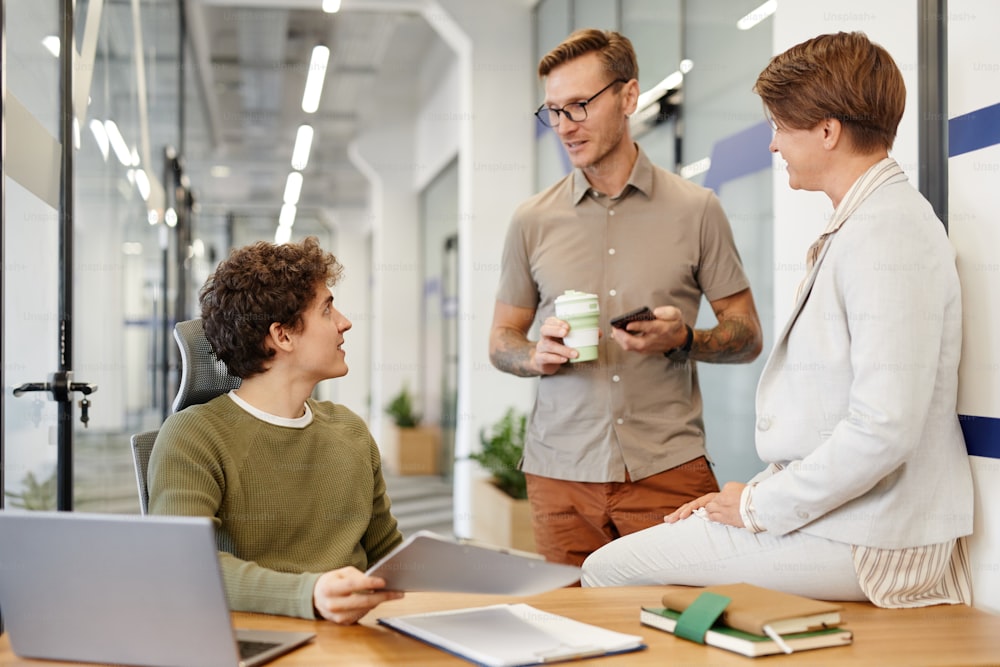 Group of young people chatting with new employee at workplace in modern office space