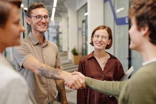 Portrait of modern business team welcoming new employee focus on smiling tattooed man shaking hands with intern