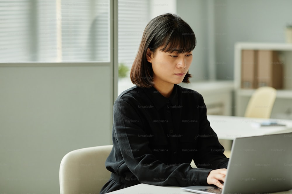 Minimal portrait of young woman using laptop while working at desk in office cubicle, copy space