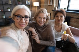 Portrait of happy senior women smiling at camera while sitting together on sofa in the living room