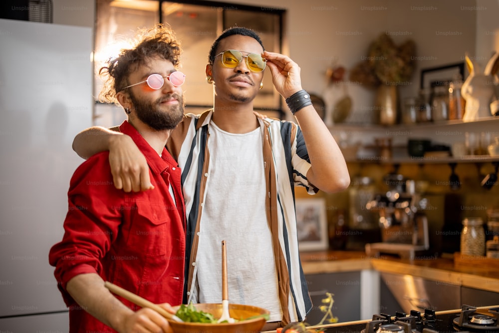 Two brightly dressed guys having fun while making salad together on kitchen. Concept of gay couples and everyday life at home. Caucasian and hispanic man cooking healthy food