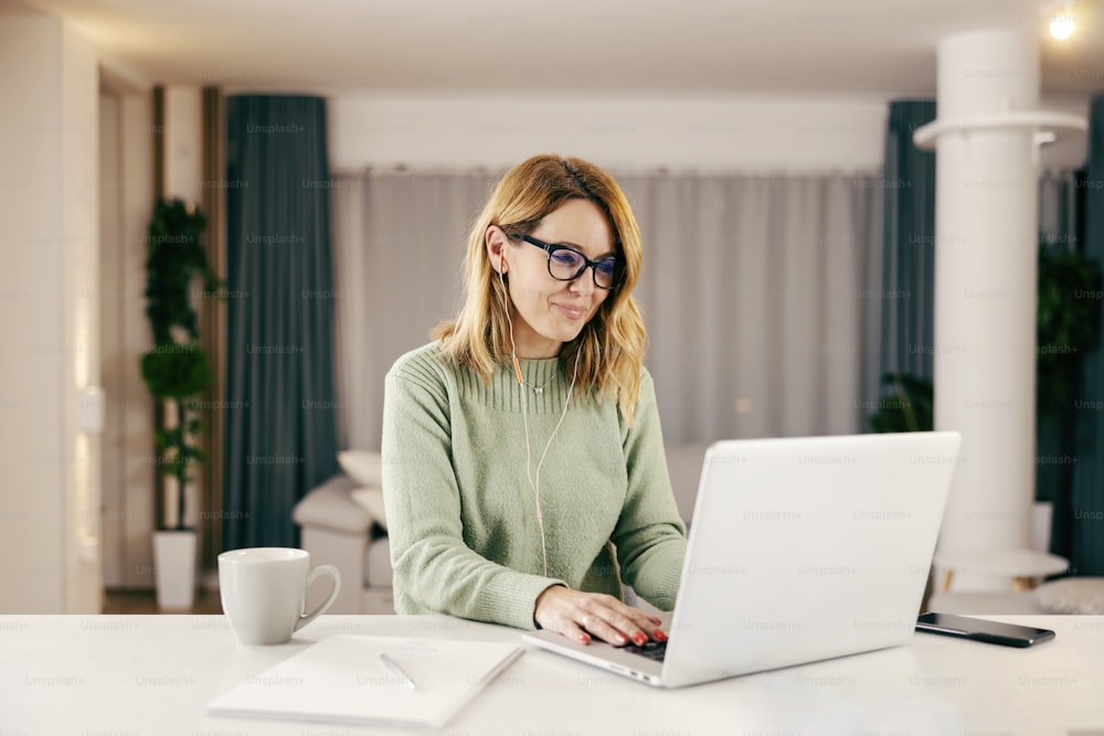 Una mujer feliz escribiendo en la computadora portátil y trabajando en línea desde casa.
