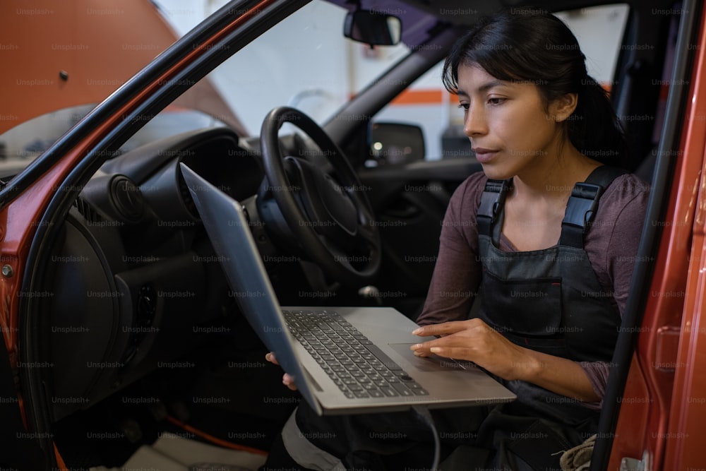 Ritratto di meccanico di auto femminile che utilizza il computer portatile durante l'ispezione del veicolo in officina di riparazione auto, spazio di copia