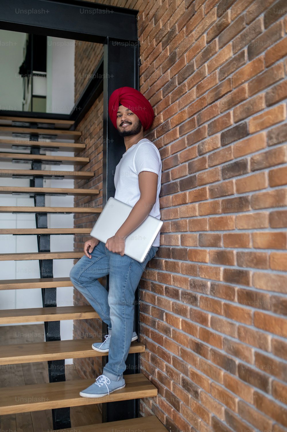 Work from home. Young indian man in red turban standing on stairs