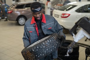 Young repairman or worker of maintenance service carrying new wheel while going to replace it in car or other vehicle