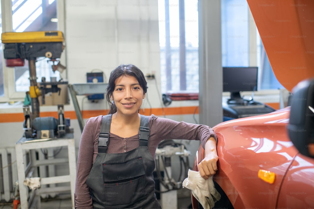 Retrato de cintura para arriba de una mecánica mirando a la cámara mientras está parada junto al automóvil en un taller de reparación de automóviles, copia el espacio