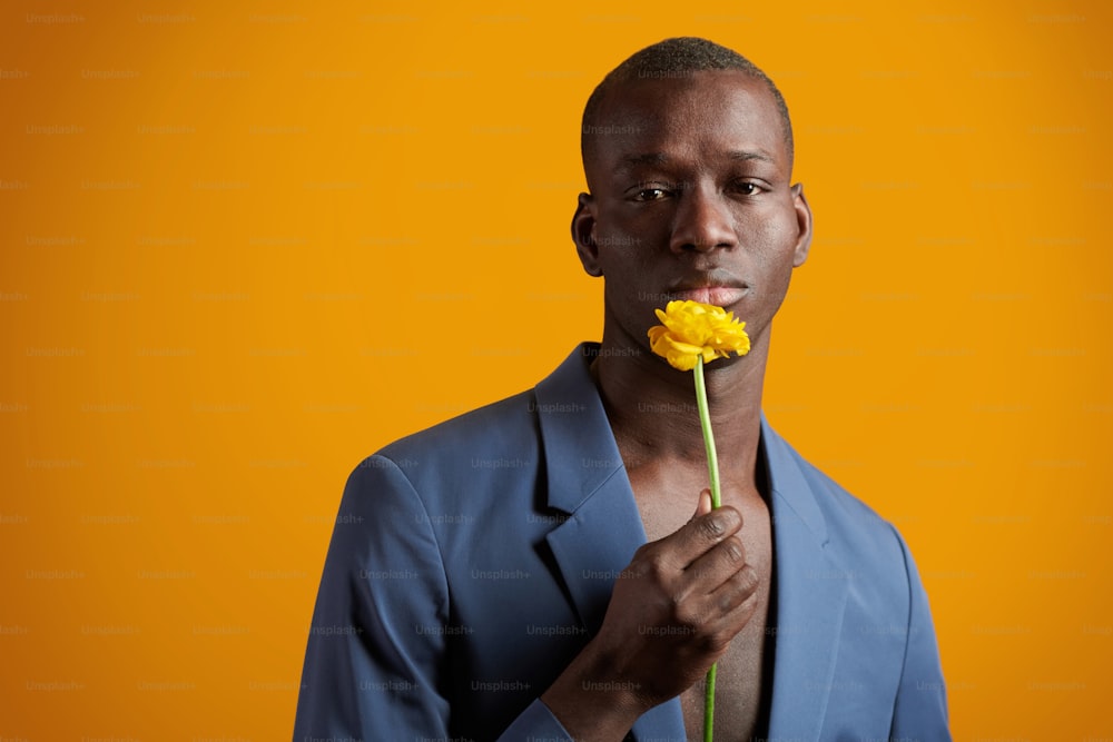 양복을 입은 아프리카 잘생긴 남자가 노란색 배경에 고립된 꽃을 들고 카메라에 포즈를 취하는 초상화