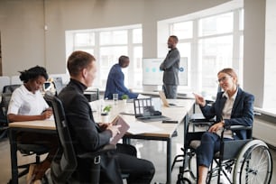 Diverse group of business people at meeting table in office with woman using wheelchair in foreground