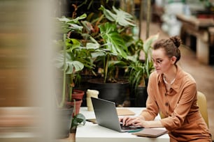 젊은 현대 여성 디자이너 또는 꽃집 노트북 앞 책상 옆에 앉아 인터넷에서 일하는 중소기업 소유자