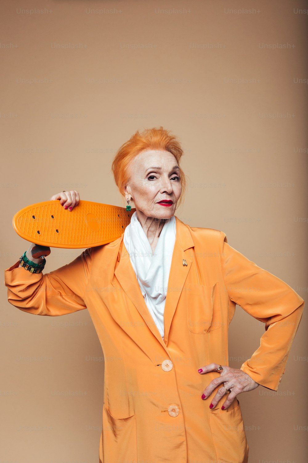 Photo of attractive mature redhead fashion woman standing isolated at studio holding skateboard. Looking at camera.