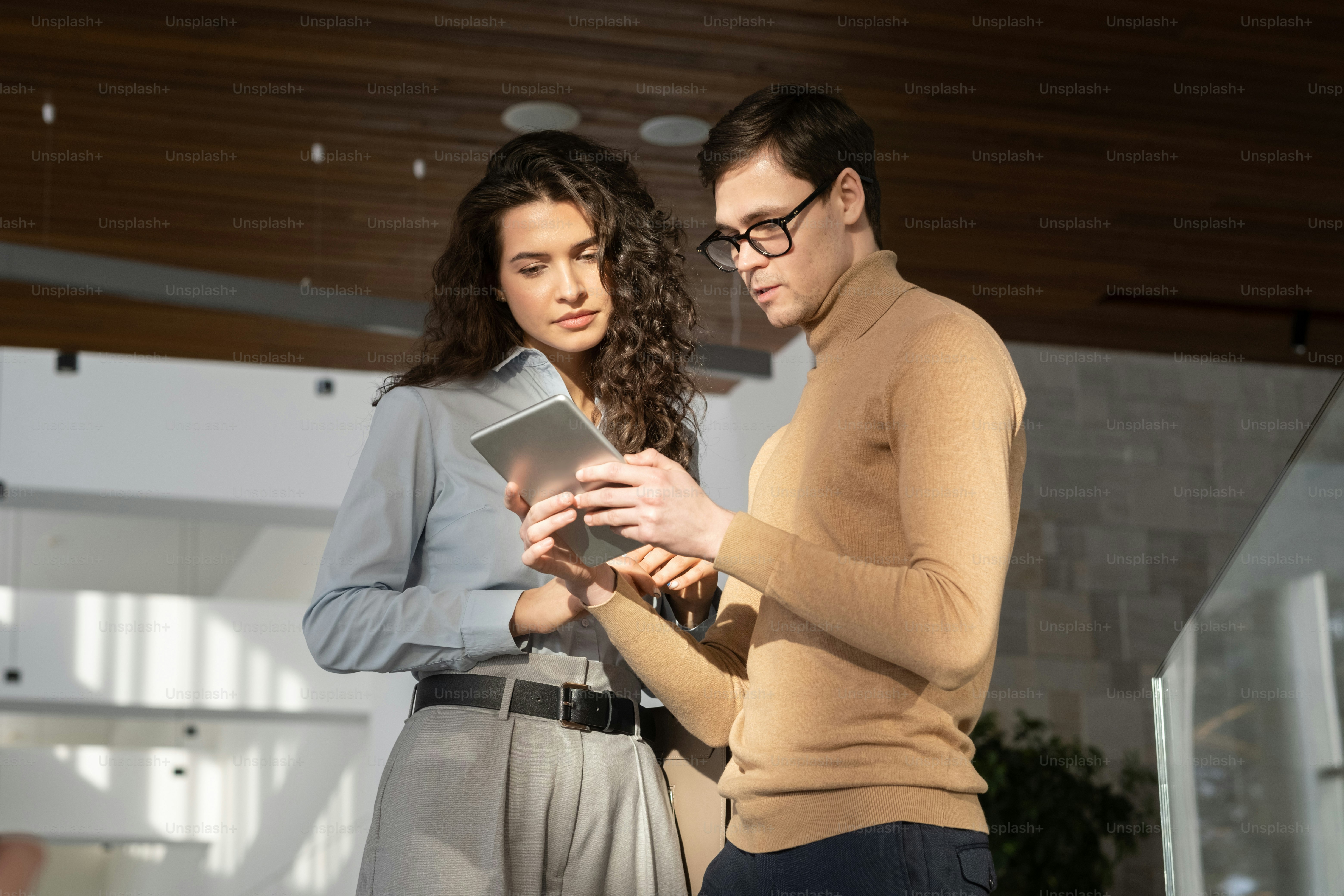 Jeune employée à l’écoute d’un collègue masculin confiant avec une tablette numérique lors d’un rapport ou d’une présentation de données d’externalisation