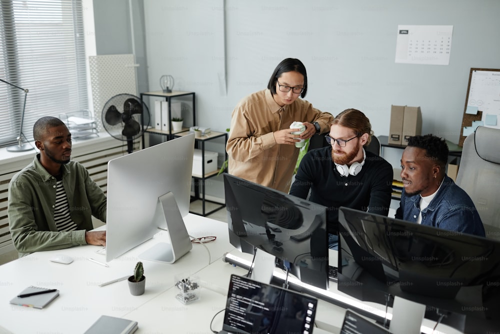 Team of young intercultural office workers in casual clothes looking at data on compute rscreen during work over data decoding