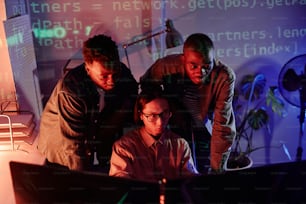 Gruppe junger interkultureller Programmierer, die sich vor Computermonitoren beugen, während sie Daten dekodieren oder neue Software entwickeln