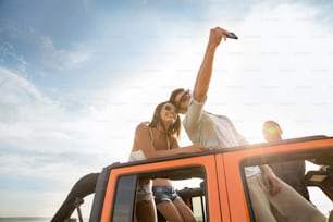 Jóvenes amigos felices tomándose selfies durante un viaje por carretera en un automóvil