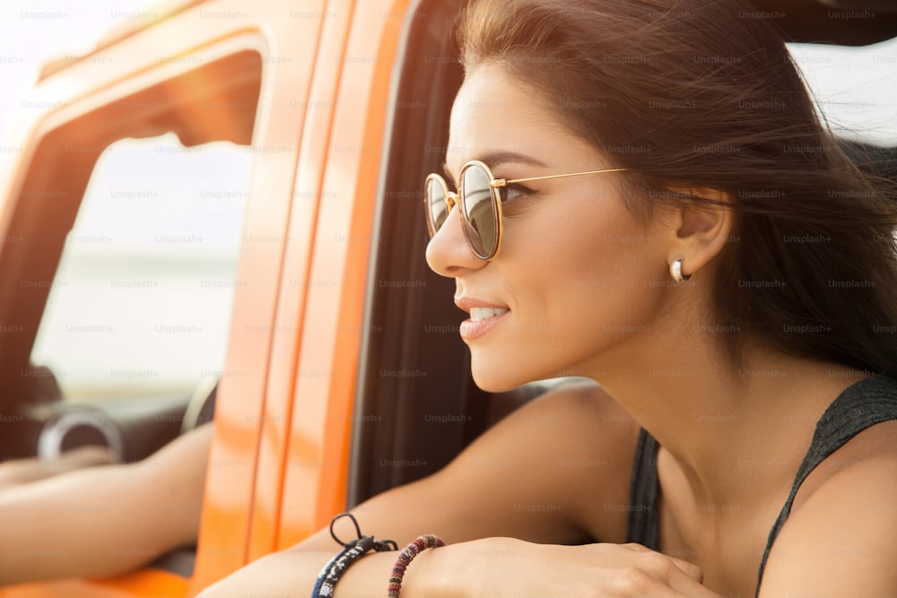 Primer plano de una mujer sonriente feliz sentada y mirando por la ventana en un automóvil
