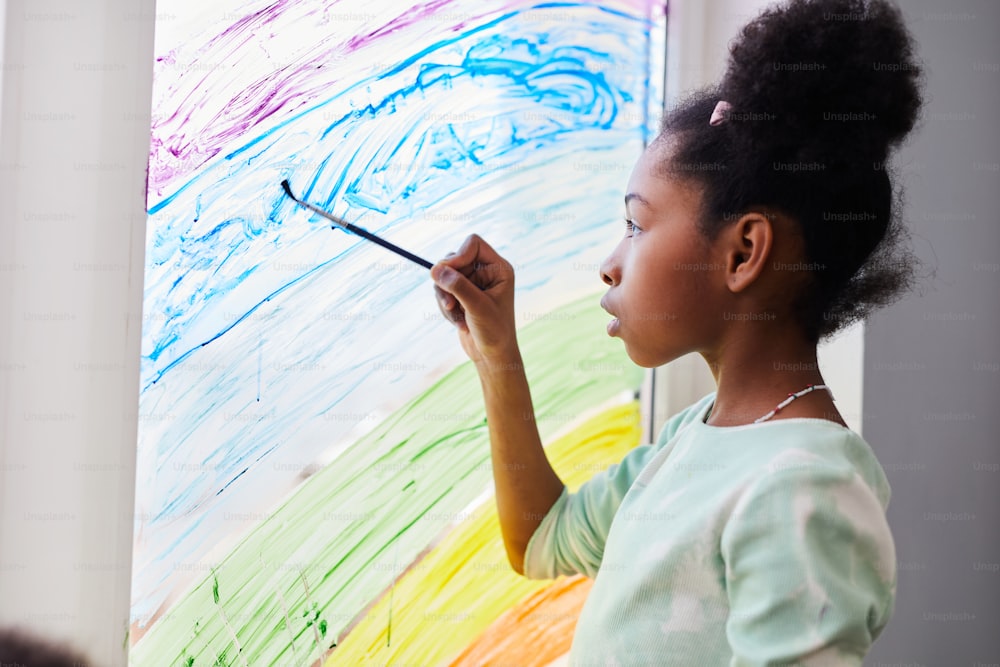 Ritratto di ragazza afro-americana che disegna con la vernice sulle finestre mentre decora la camera da letto del bambino, spazio di copia