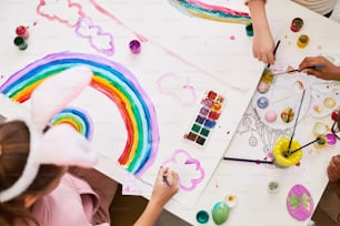 Top view portrait of little girl drawing rainbow at art and craft table while enjoying Easter party for children