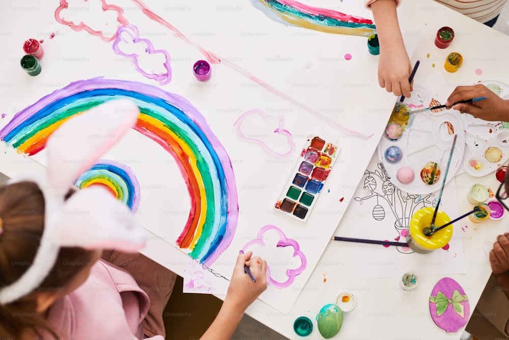 Top view portrait of little girl drawing rainbow at art and craft table while enjoying Easter party for children