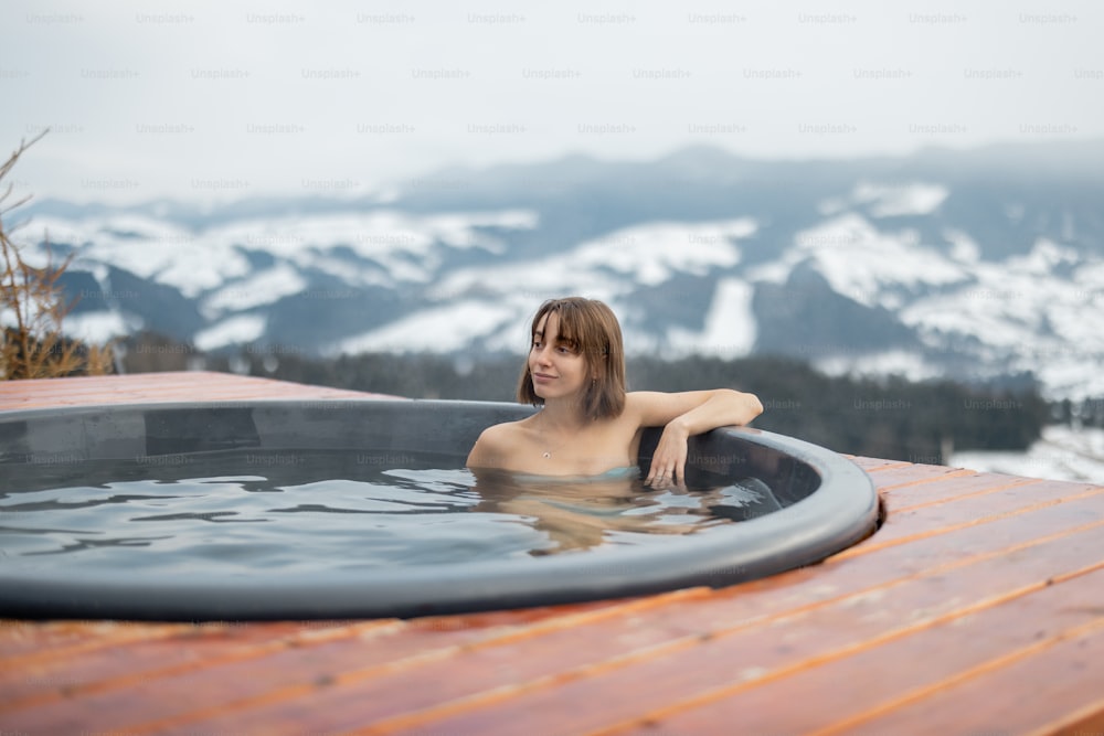 Giovane donna che fa il bagno nella vasca idromassaggio in montagna durante l'inverno. Concetto di riposo e recupero in vasca calda sulla natura. Idea di fuga e svago sulle montagne