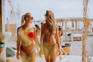 Pretty young women in bikini walking by the surf cabin on a beach at summer day