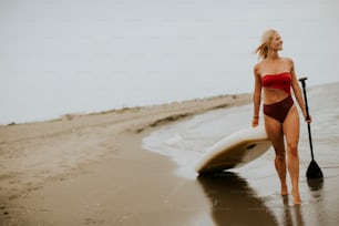 Pretty young woman walking with paddle board on the beach on a summer day