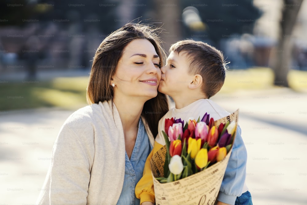 Ein kleiner Junge, der seiner Mutter einen Tulpenstrauß schenkt und sie am Muttertag küsst.