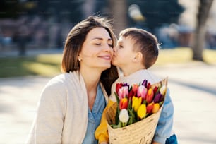 A little boy giving bouquet of tulips to his mother and kissing her on mother's day.