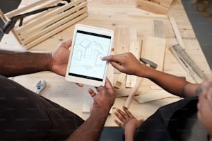 Top view close up of father and son building birdhouse together and looking at plans on digital table