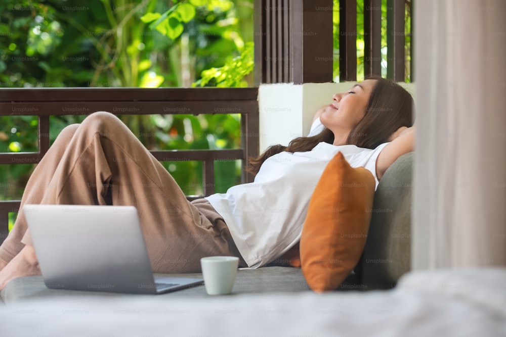 Immagine ritratto di una giovane donna sdraiata sul divano con computer portatile e tazza di caffè