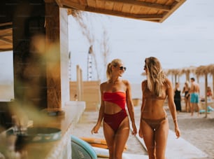Mujeres jóvenes guapas en bikini caminando por la cabaña de surf en una playa en un día de verano