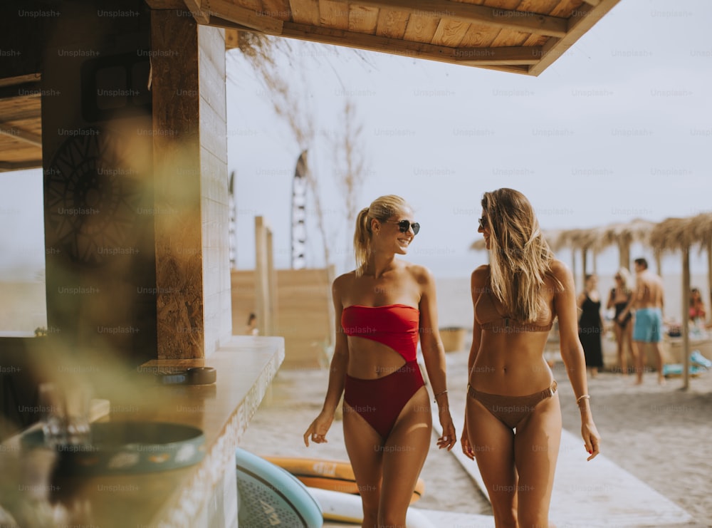 Hübsche junge Frauen im Bikini gehen an einem Sommertag an der Surfhütte am Strand vorbei