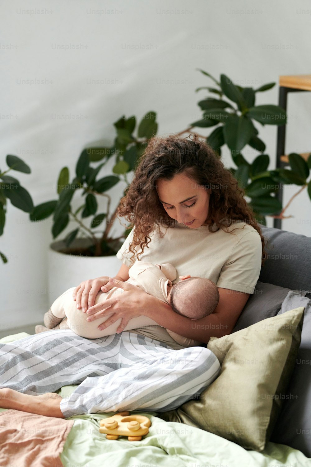 Junge Mutter in Hauskleidung, die sich durch Kissen auf einem Doppelbett im Schlafzimmer entspannt und ihren süßen kleinen Sohn einschläfert